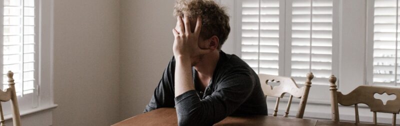 man sitting at the table, covering his face - suffering from depression